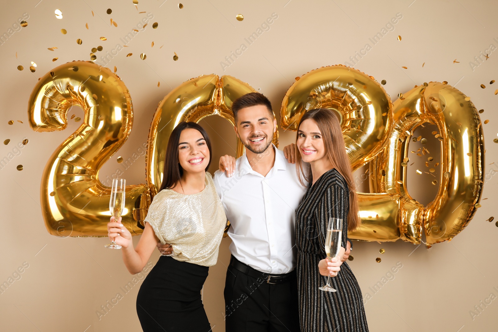 Photo of Happy young friends near golden 2020 balloons on beige background. New Year celebration