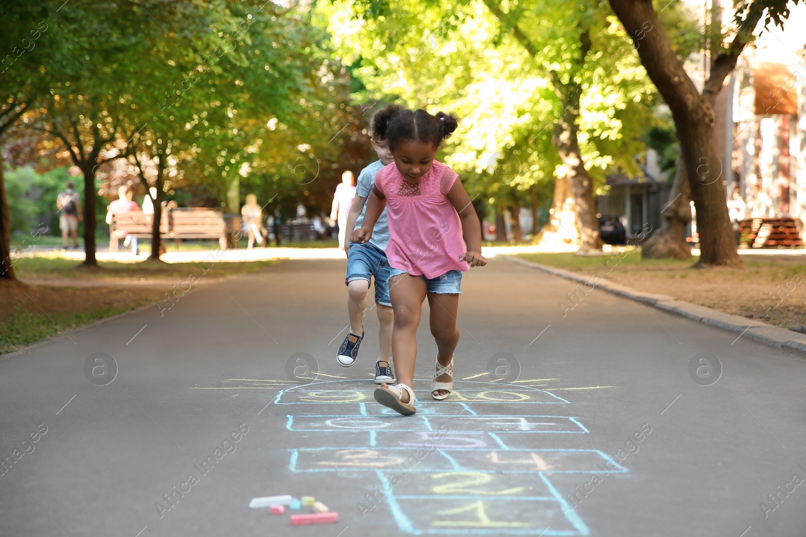 Photo of Little children playing hopscotch drawn with colorful chalk on asphalt