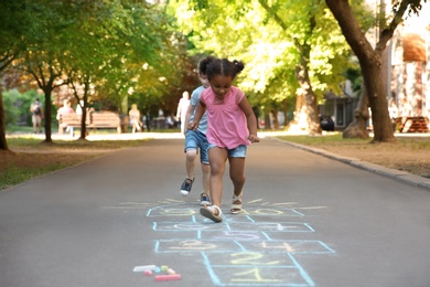 Photo of Little children playing hopscotch drawn with colorful chalk on asphalt