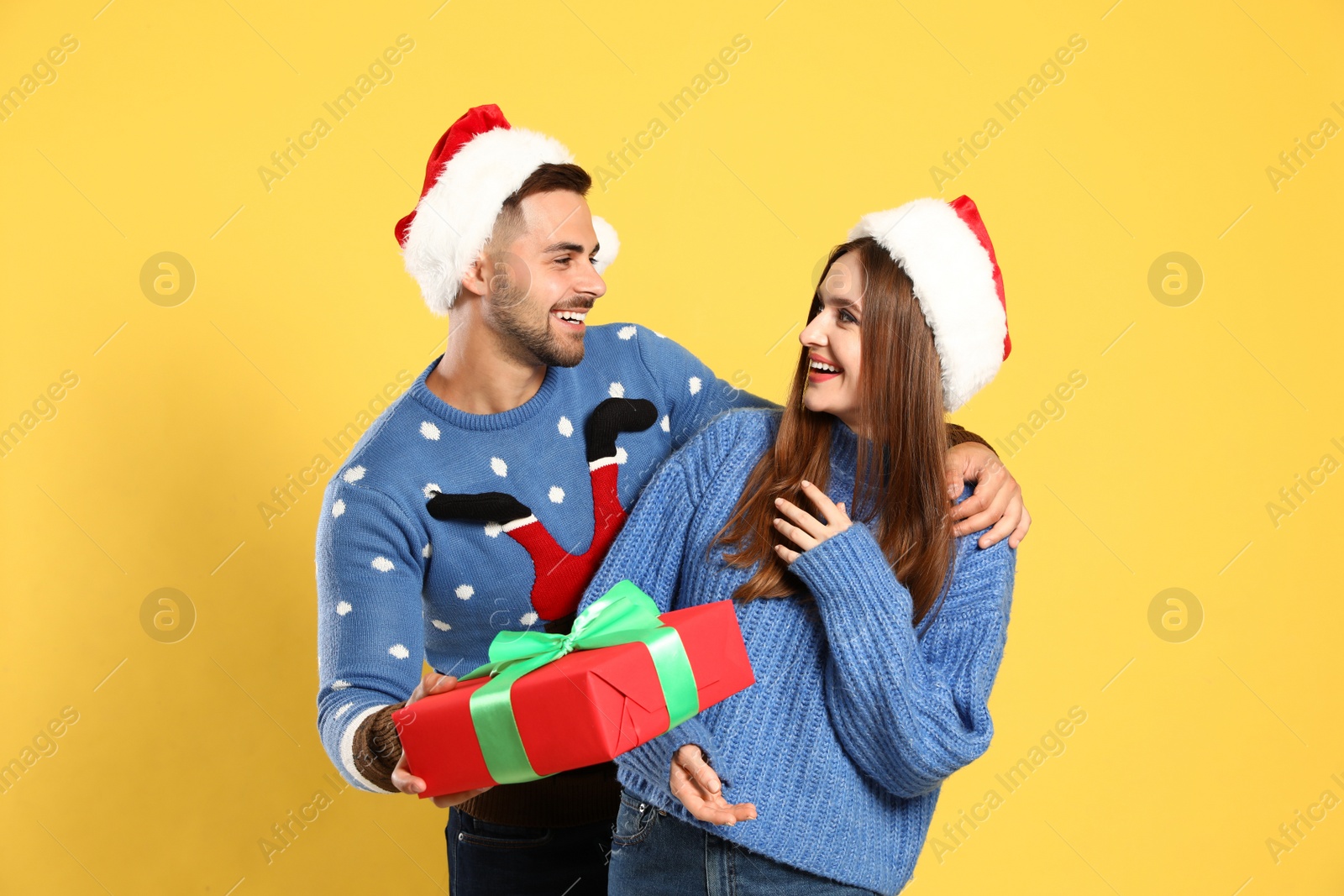 Photo of Couple wearing Christmas sweaters and Santa hats on yellow background