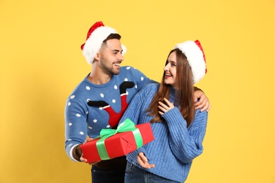 Couple wearing Christmas sweaters and Santa hats on yellow background