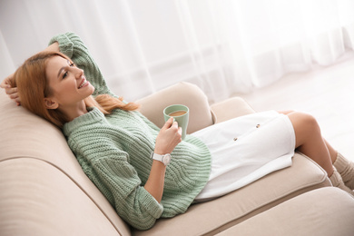 Photo of Young woman with cup of drink relaxing on couch at home