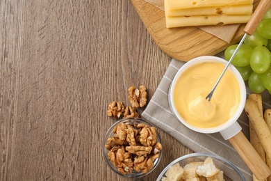 Photo of Flat lay composition with pot of tasty cheese fondue on wooden table, space for text