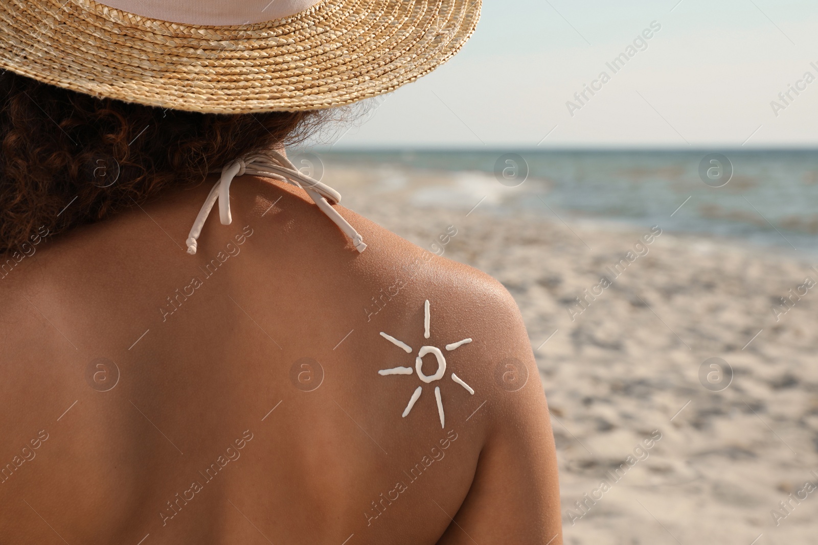 Photo of African American woman with sun protection cream on shoulder at beach, back view