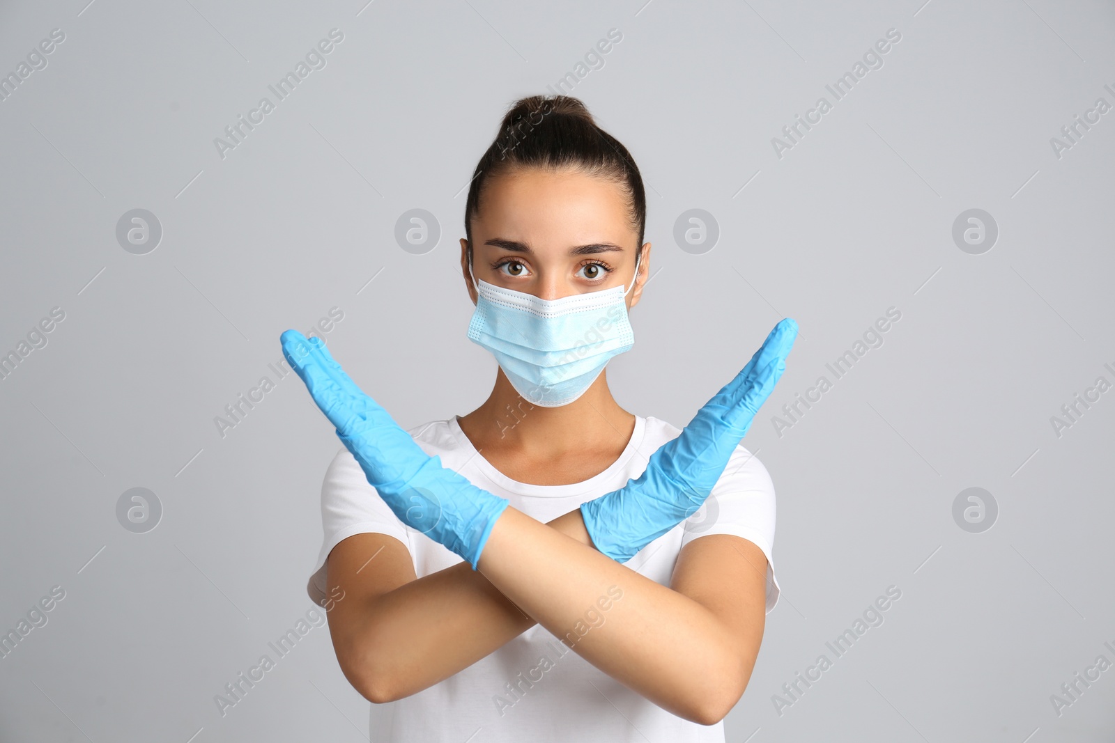 Photo of Woman in protective mask showing stop gesture on grey background. Prevent spreading of COVID‑19