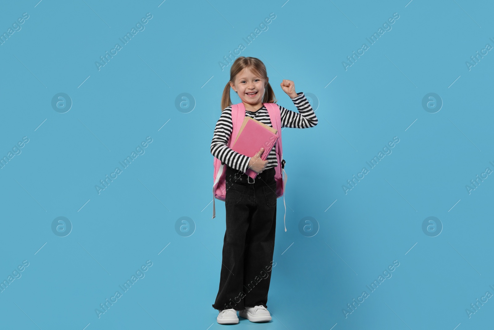 Photo of Happy schoolgirl with backpack and books on light blue background