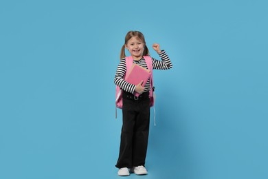 Happy schoolgirl with backpack and books on light blue background