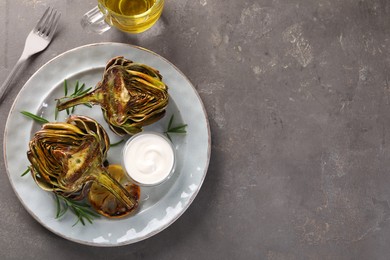 Photo of Plate with tasty grilled artichoke served on grey table, flat lay. Space for text