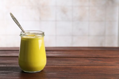 Tasty mustard sauce and spoon in glass jar on wooden table, space for text