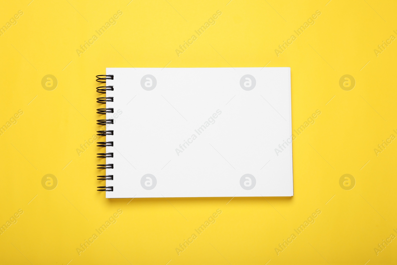 Photo of Open blank notebook on yellow background, top view