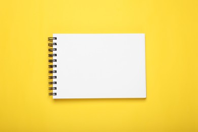 Open blank notebook on yellow background, top view