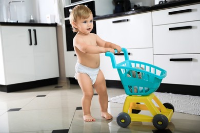 Photo of Cute baby with toy walker in kitchen. Learning to walk