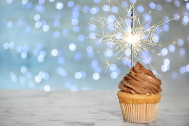 Birthday cupcake with sparkler on table against blurred lights. Space for text