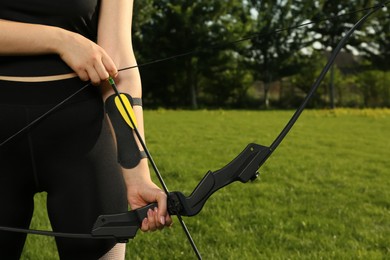 Photo of Woman with bow and arrow practicing archery in park, closeup