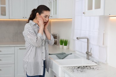 Image of Shocked woman looking at affected with mold countertop in kitchen