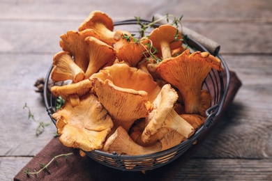 Photo of Fresh wild chanterelle mushrooms in metal basket on wooden table, closeup