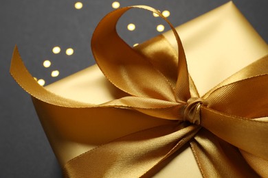 Photo of Golden gift box with bow on black background, closeup