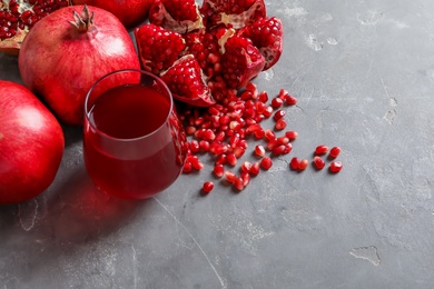 Photo of Glass of pomegranate juice and fresh fruits on grey background, space for text