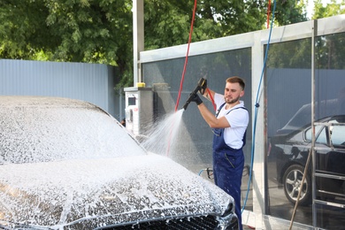 Young worker cleaning automobile with high pressure water jet at car wash