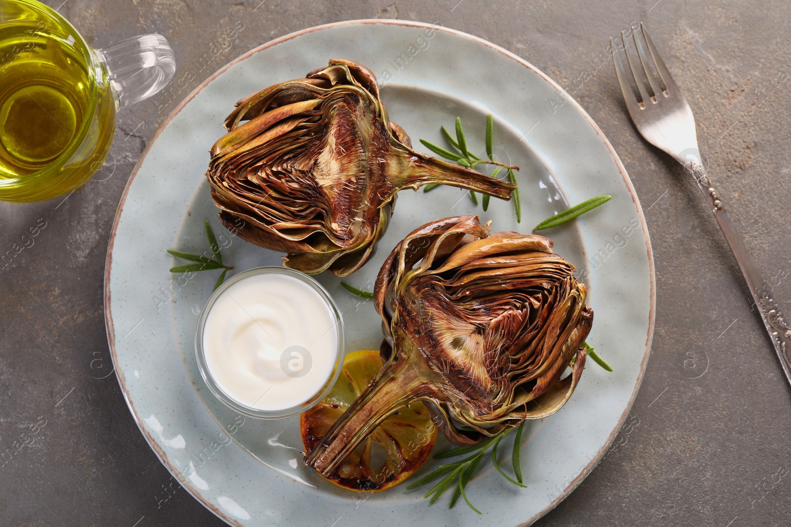 Photo of Plate with tasty grilled artichoke served on grey table, flat lay