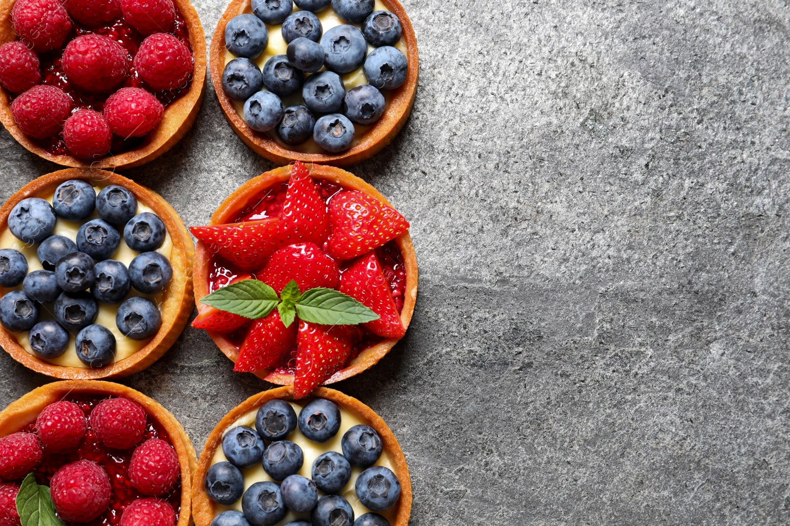 Photo of Tartlets with different fresh berries on light grey table, flat lay and space for text. Delicious dessert