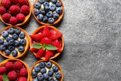 Photo of Tartlets with different fresh berries on light grey table, flat lay and space for text. Delicious dessert