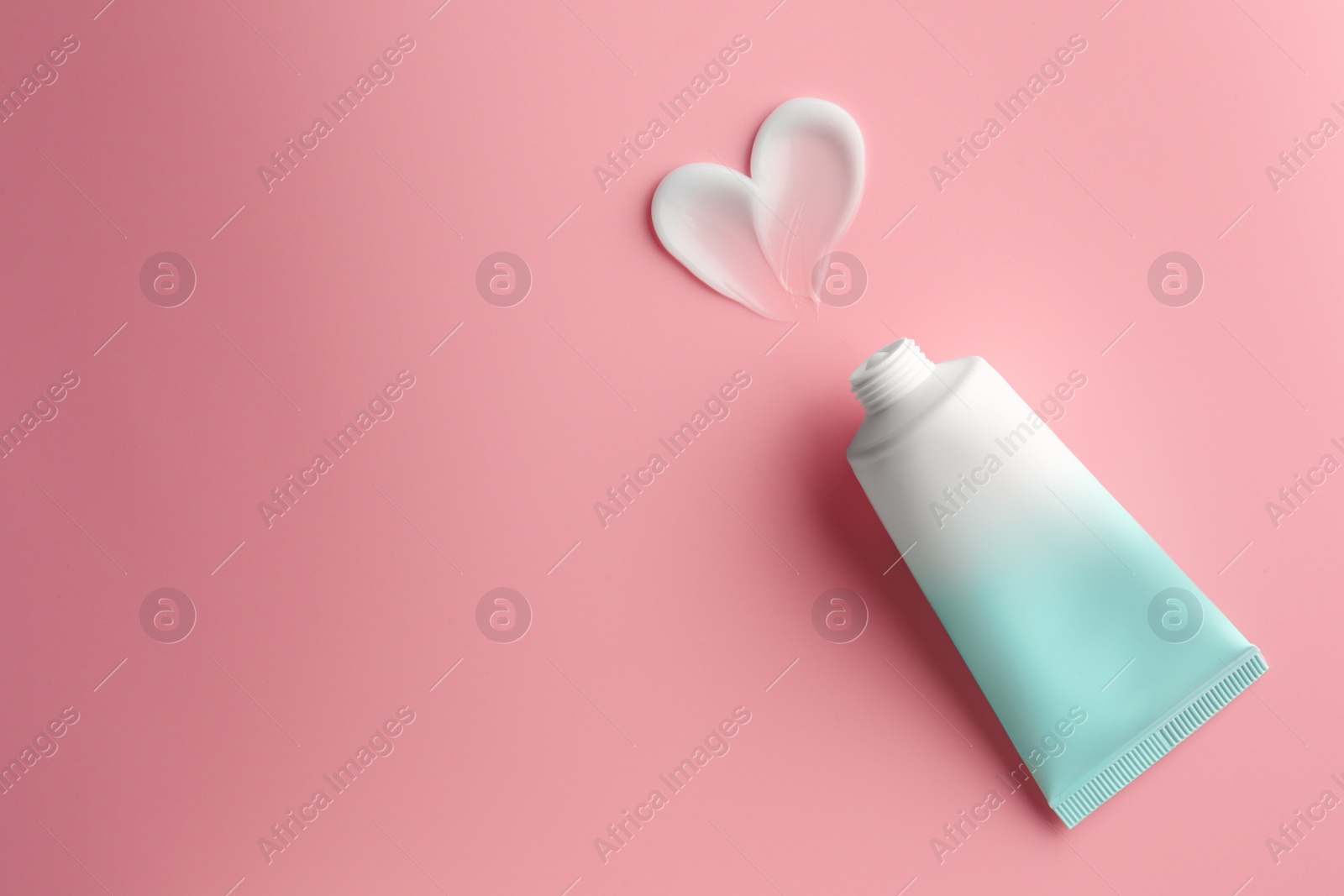 Photo of Tube and sample of facial cream on pink background, top view. Space for text