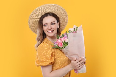 Happy young woman in straw hat holding bouquet of beautiful tulips on yellow background