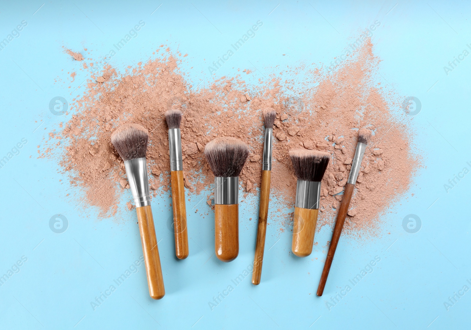 Photo of Brushes and scattered face powder on light blue background, flat lay