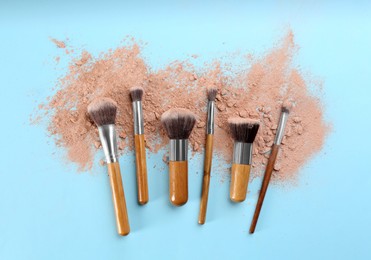 Photo of Brushes and scattered face powder on light blue background, flat lay