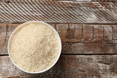 Raw basmati rice in bowl on wooden table, top view. Space for text