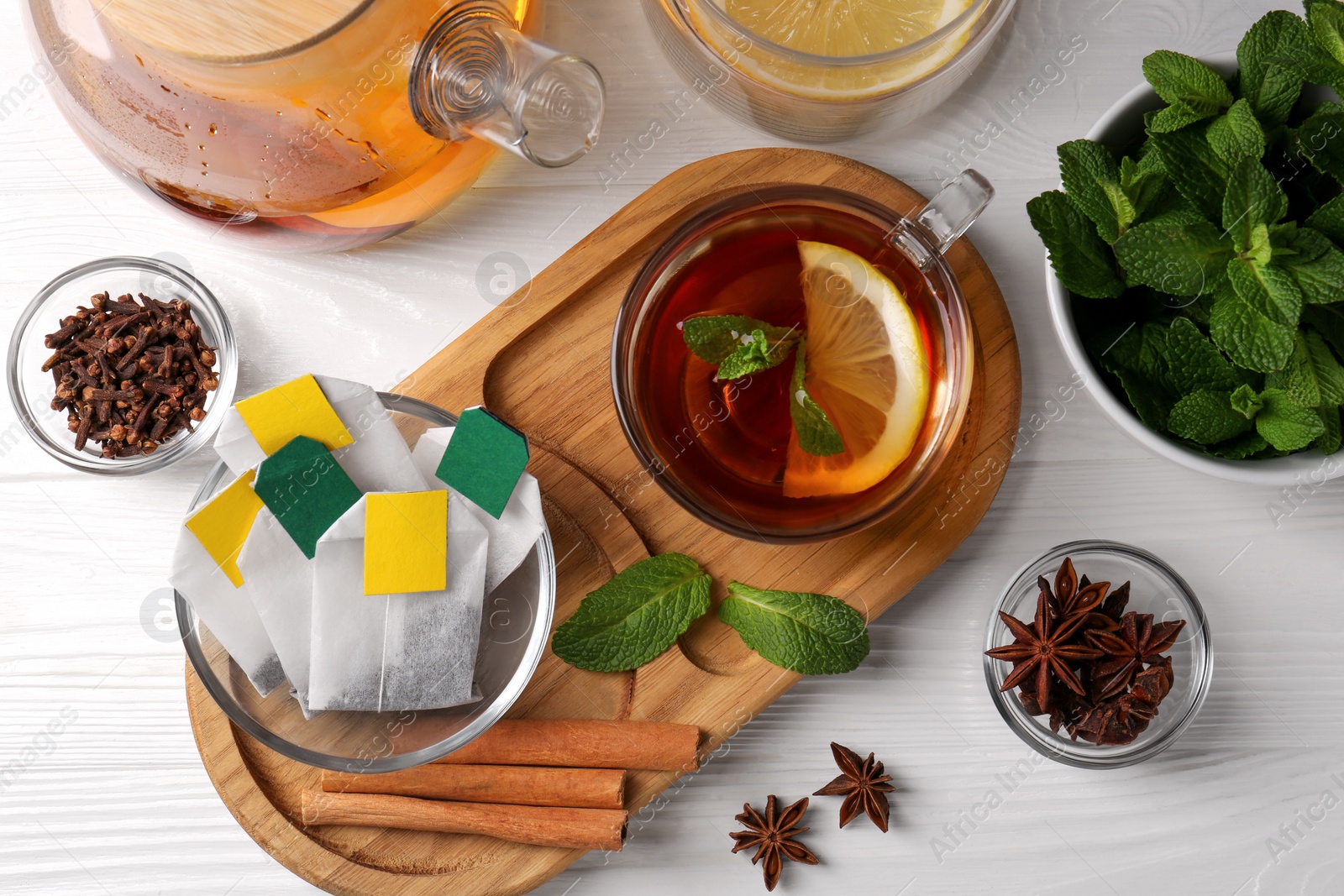 Photo of Tea bags, cup of hot drink and ingredients white wooden table, flat lay