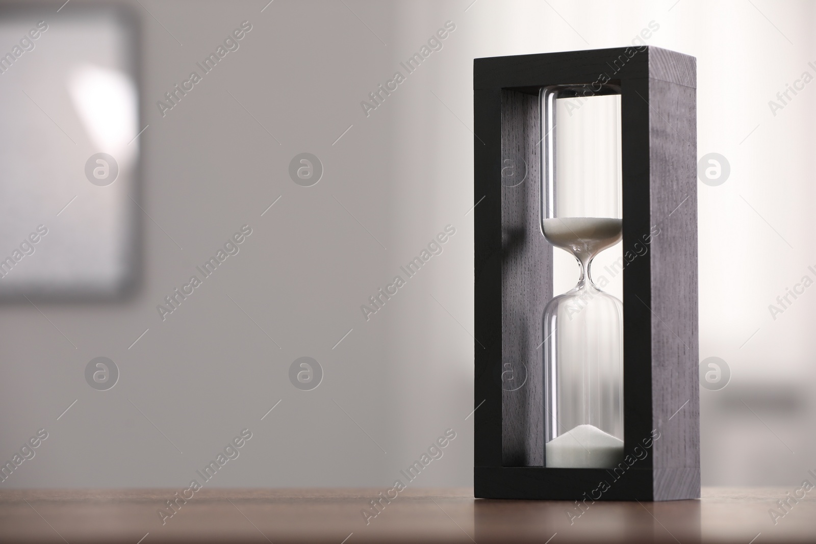 Photo of Hourglass with flowing sand on table against blurred background. Space for text