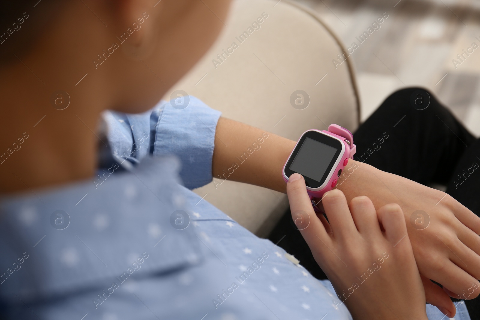 Photo of Girl using stylish smart watch on sofa indoors, closeup