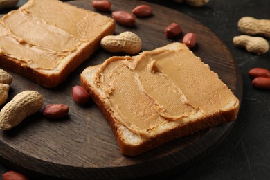 Photo of Tasty peanut butter sandwiches and peanuts on black table, closeup