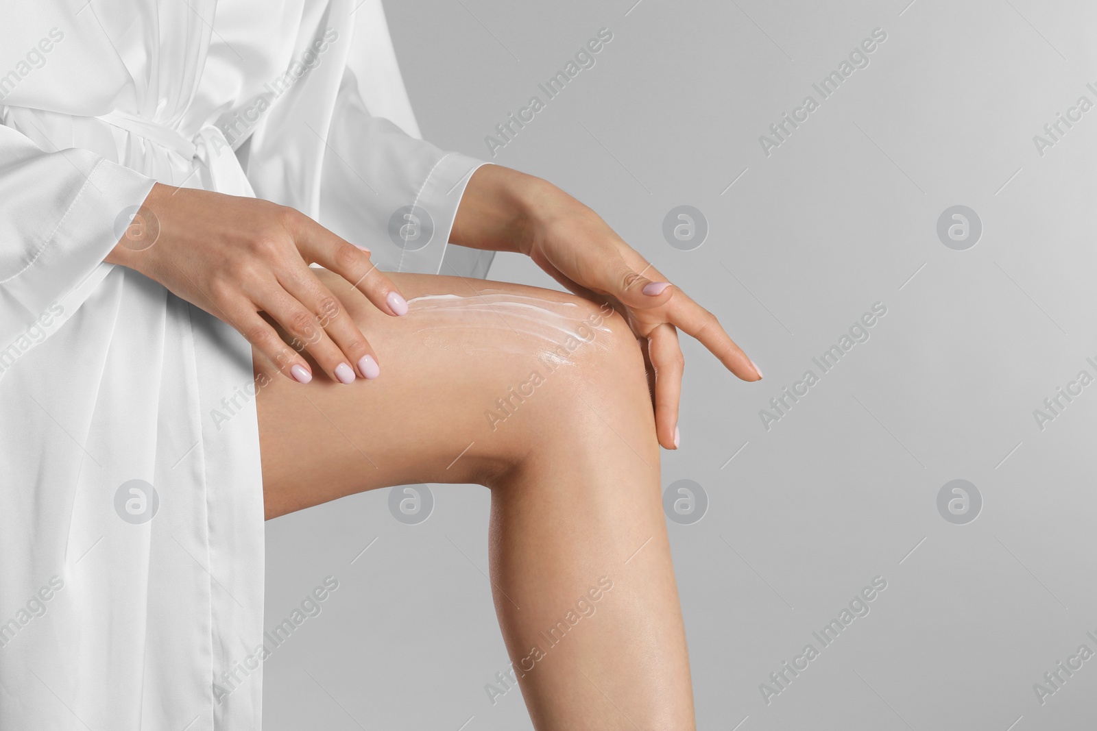 Photo of Woman applying body cream onto her smooth legs on light grey background, closeup. Space for text