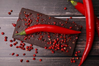 Delicious chocolate, fresh chili and red peppercorns on wooden table, flat lay