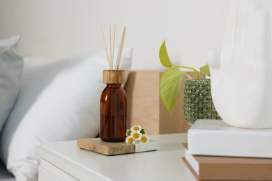 Aromatic reed air freshener, chamomiles and houseplant on white table in bedroom