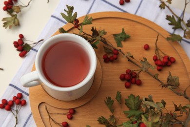 Cup with hawthorn tea and berries on beige table, above view