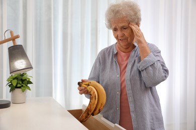 Photo of Senior woman finding bananas in chest of drawers at home. Age-related memory impairment