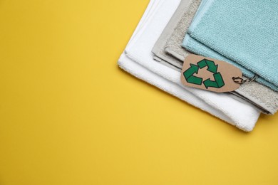 Photo of Stacked towels with recycling label on yellow background, top view. Space for text