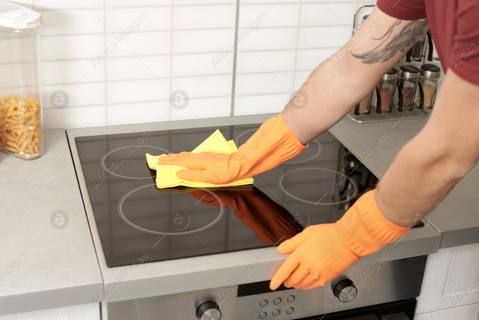 Photo of Young man cleaning oven cooktop with rag in kitchen, closeup