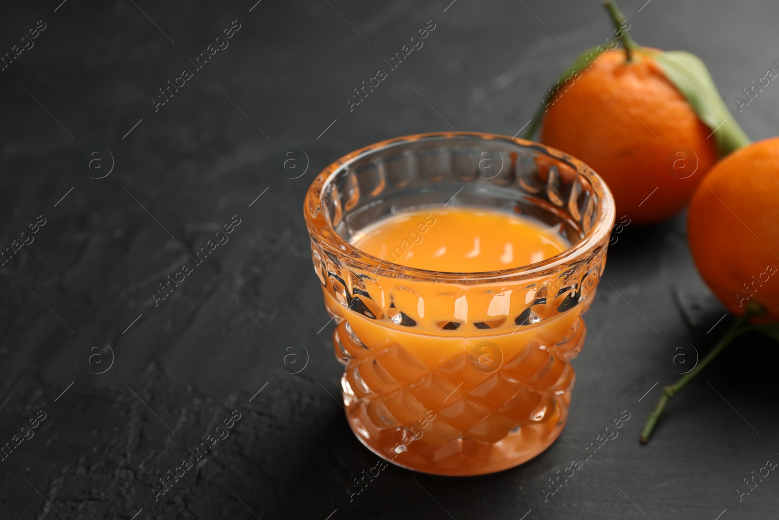 Photo of Tasty tangerine liqueur in glass and fresh fruits on black textured table, closeup. Space for text