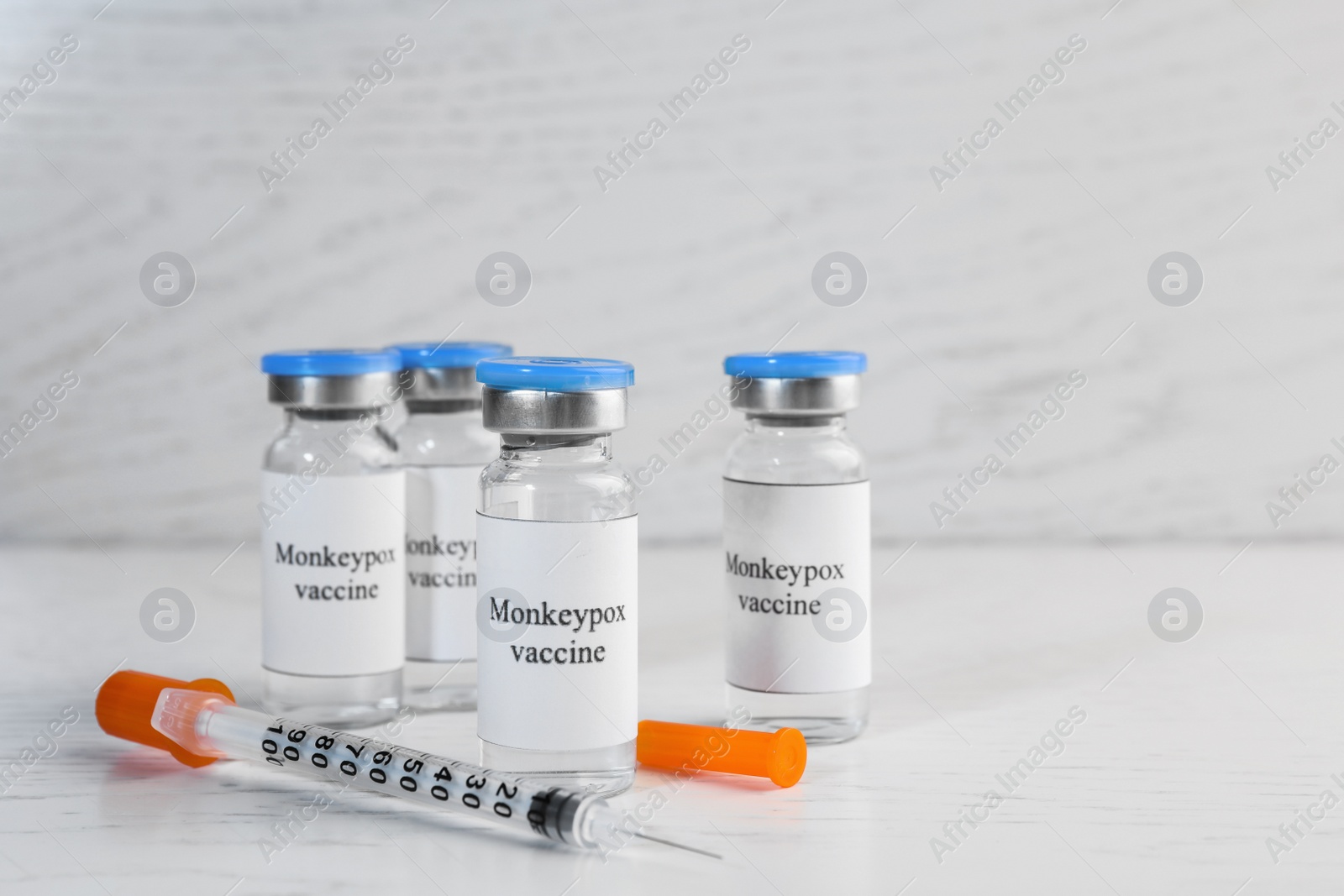 Photo of Monkeypox vaccine in glass vials and syringe on white wooden table, space for text