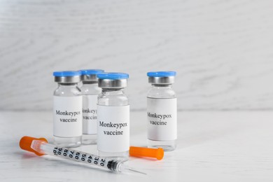Photo of Monkeypox vaccine in glass vials and syringe on white wooden table, space for text