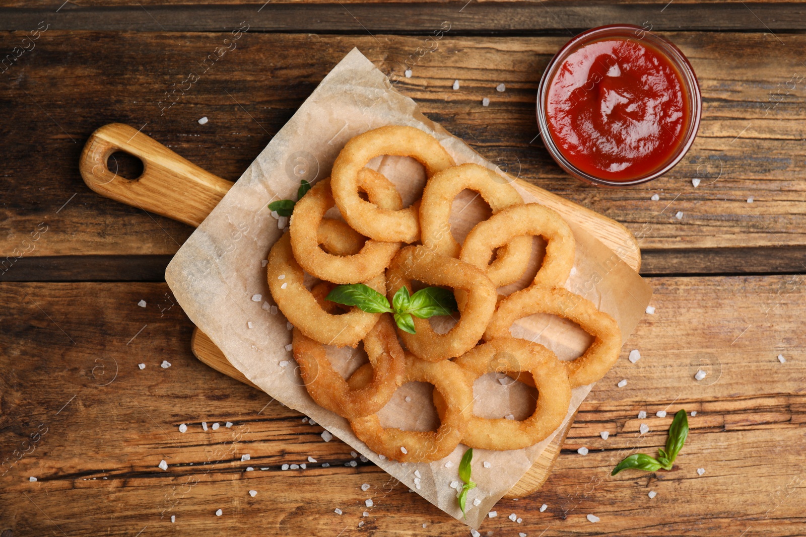 Photo of Delicious onion rings and ketchup on wooden table, flat lay