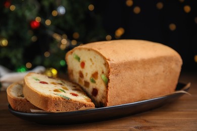 Photo of Delicious cake with candied fruits on wooden table against Christmas lights