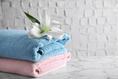 Photo of Stack of clean soft bath towels and beautiful flower on white marble table. Space for text