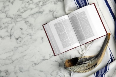 Photo of Tallit, shofar and open Torah on white marble table, flat lay with space for text. Rosh Hashanah celebration