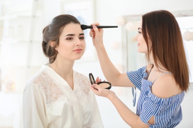 Photo of Professional makeup artist working with young woman in salon